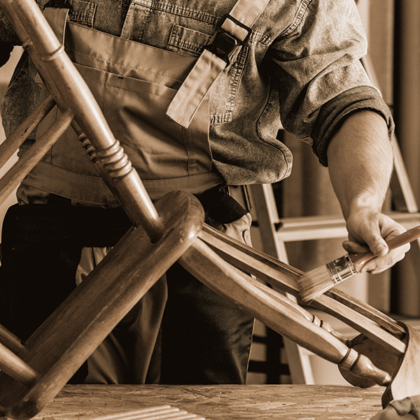 Ein Schreiner streicht bzw. renoviert einen alten Holzstuhl